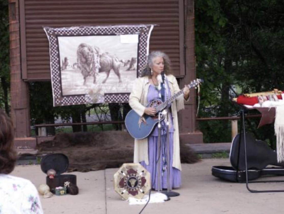 Bunny performing live outdoors with guitar and buffalo tapestry